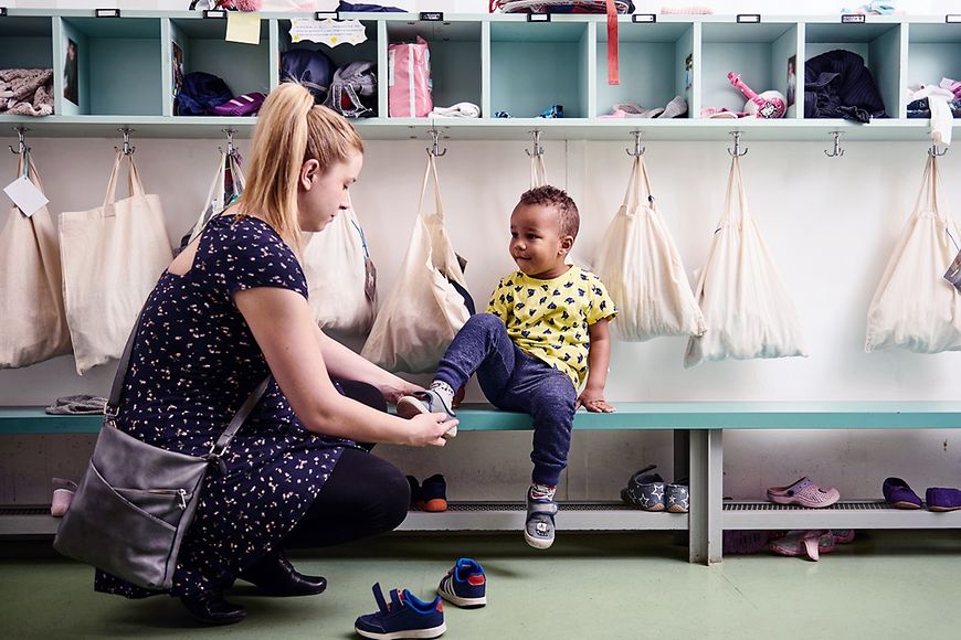 Kita: Mutter zieht einem Kleinkind die Schuhe an