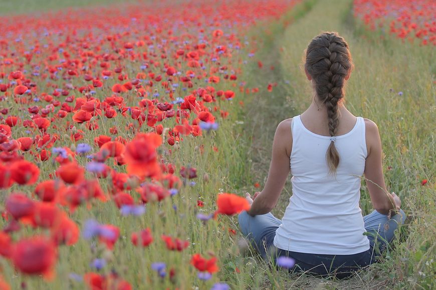 Frau sitzt in einem Mohnblumenfeld in Yogahaltung