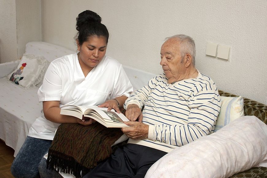 Pflegekraft - weiblich - schaut sich mit älteren Herrn ein Buch an