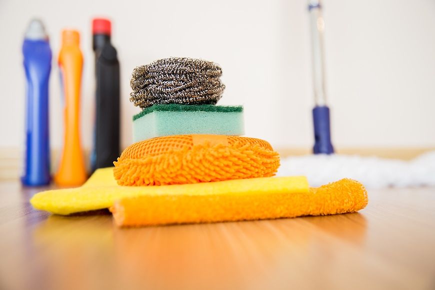 Zwei Hände mit Haushaltshandschuhen, Lappen und Sprühflasche