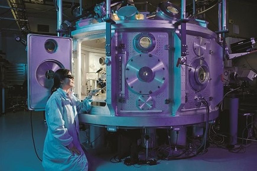 Wissenschaftlerin mit Schutzbrille schaut in ein großes technisches Gerät