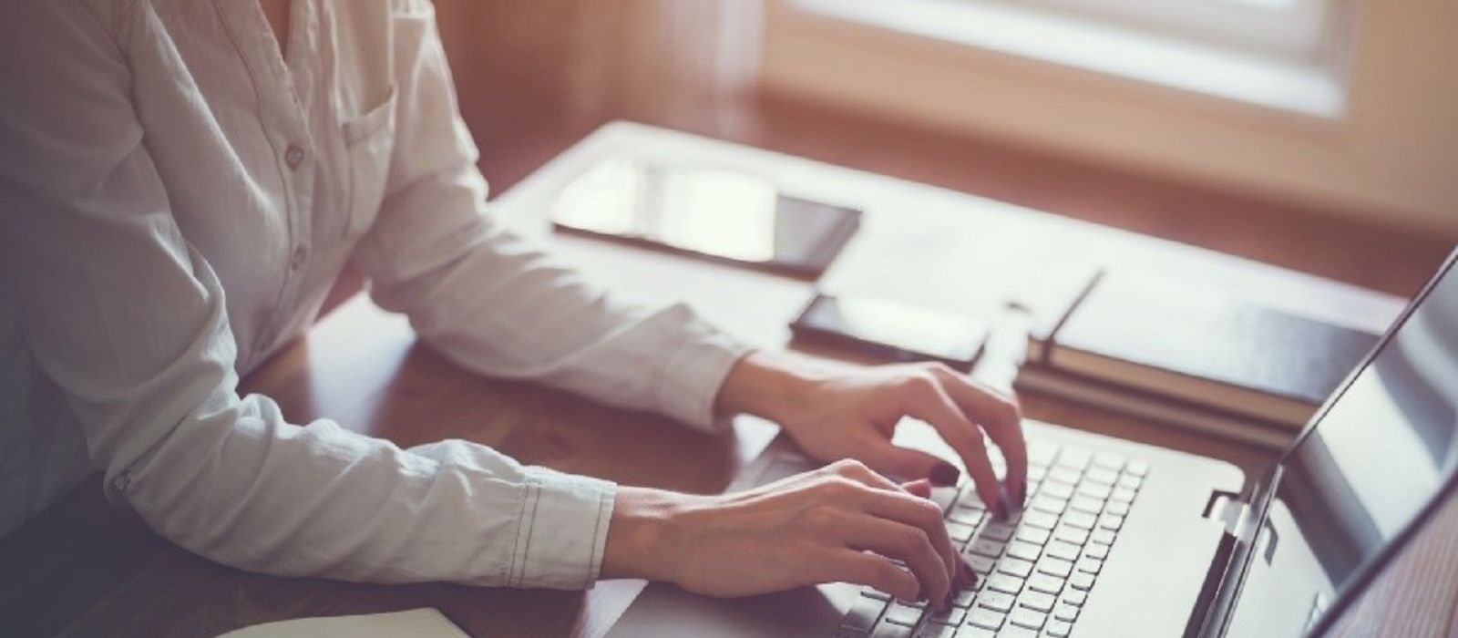 Frau am Schreibtisch, Hände auf einer Laptoptastatur