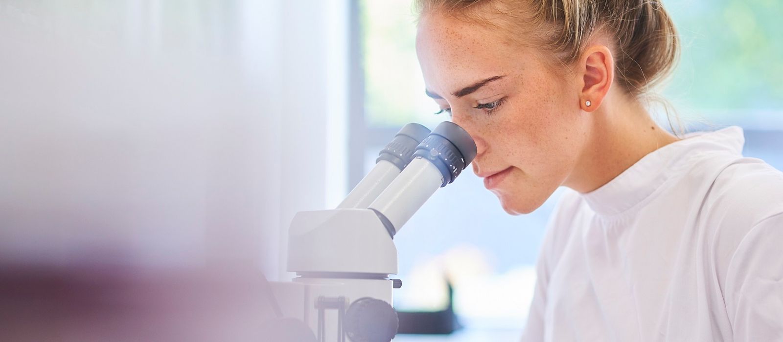 Frau im Labor, weißer Kittel, sitzt am Mikroskop