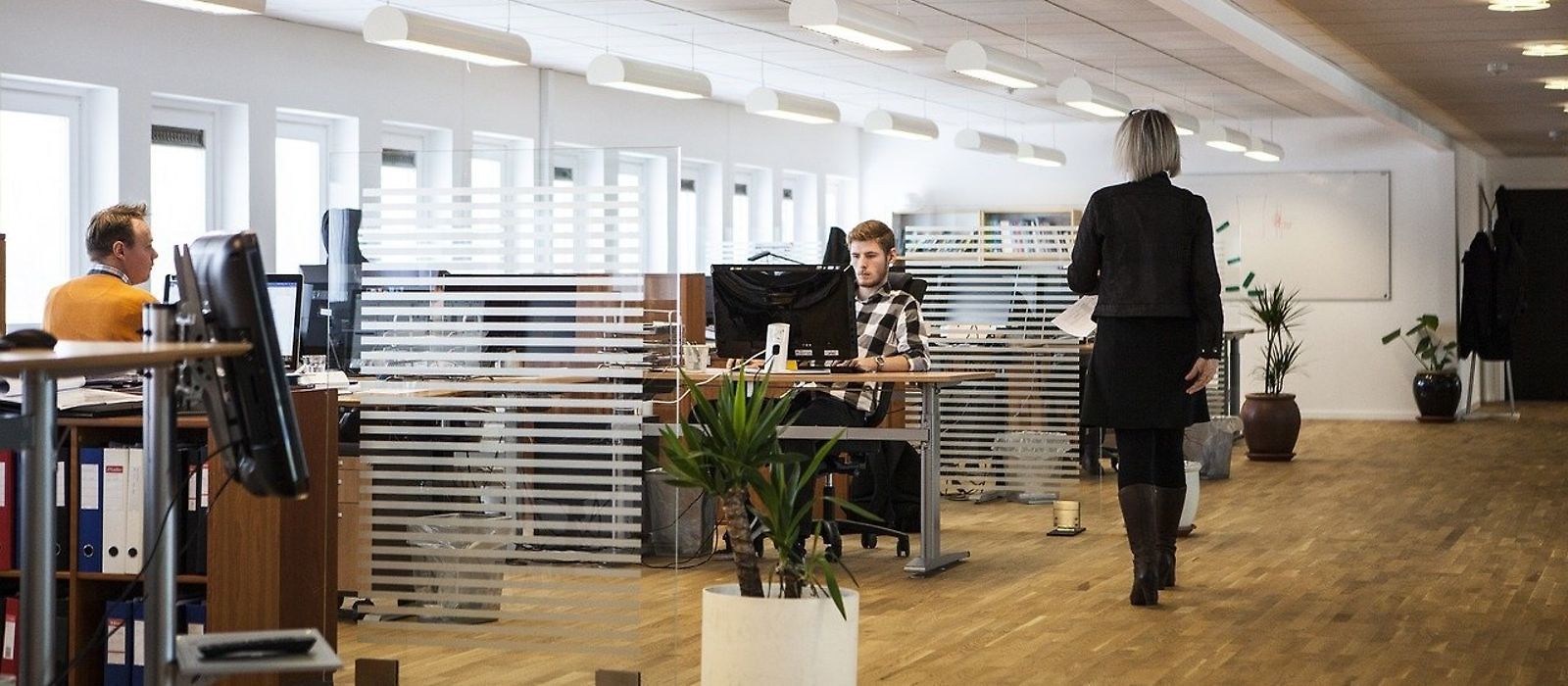 Großraumbüro - zwei Männer am Arbeitplatz - eine Frau geht durch den Raum
