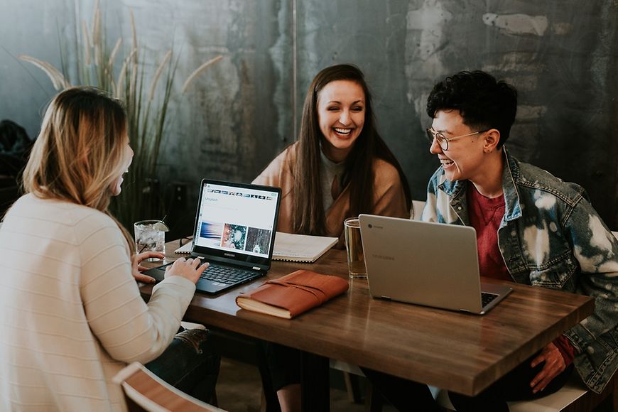 Zwei Frauen, ein Mann am Schreibtisch mit Laptops - gute Stimmung