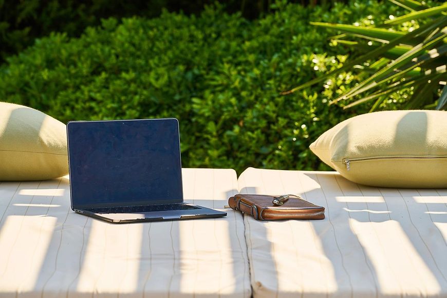 Aufgeklappter Laptop, Tasche, zwei Kissen auf einer Sitzgelegenheit im Freien