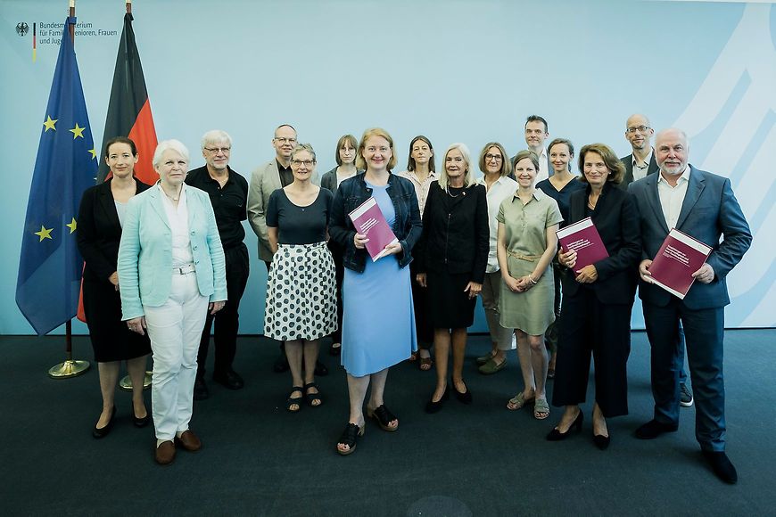 Mehrere Personen u. a. Lisa Paus stehen vor einer Pressewand mit Publikationen in der Hand