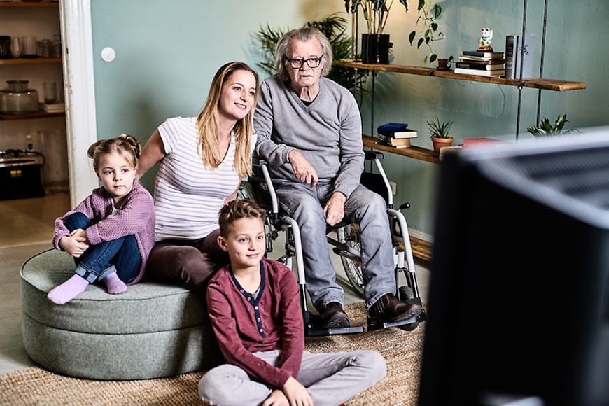 Junge, Mädchen, Frau und Mann im Rollstuhl schauen Fernsehen
