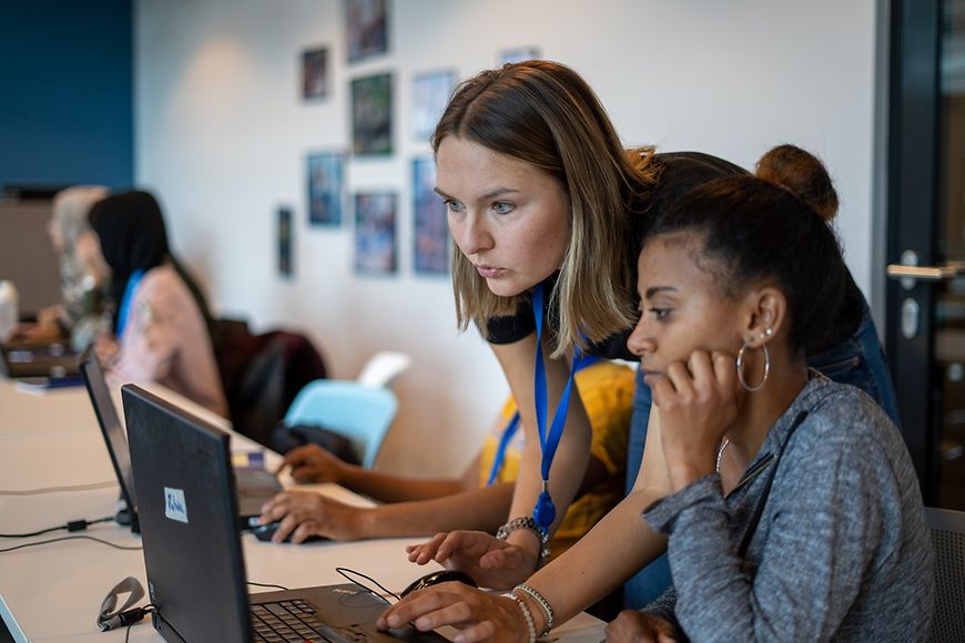 Unterrichtsraum: zwei Frauen im Vordergrund - schauen auf einen Laptop