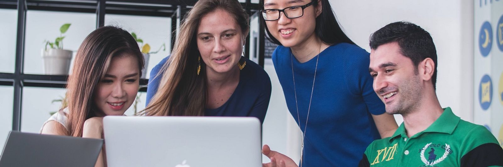 Drei junge Frauen und ein junger Mann schauen gemeinsam auf einen Laptop