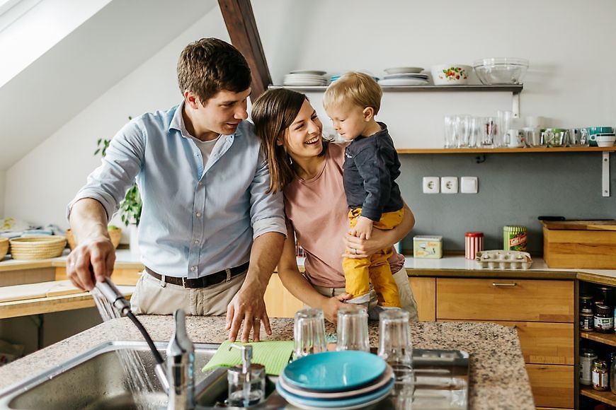 Eine Familie mit Vater, Mutter und Kind steht in einer Küche an der Spüle.