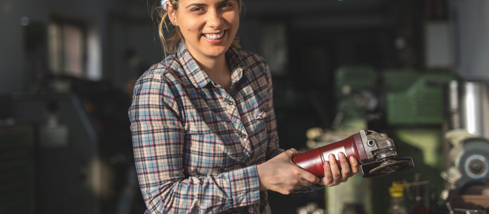 Junge Frau hält ein Werkzeug in der Hand und lächelt