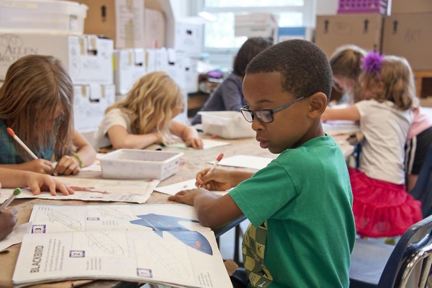 Grundschule: Junge sitz mit anderen Kindern am Tisch, alle malen