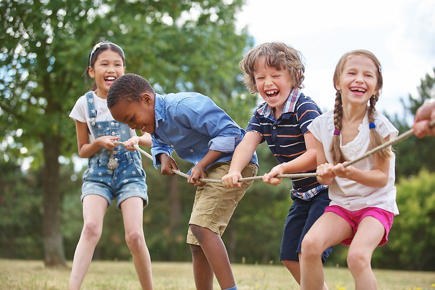 Kinder spielen draußen mit einem Seil Tauziehen und lachen 