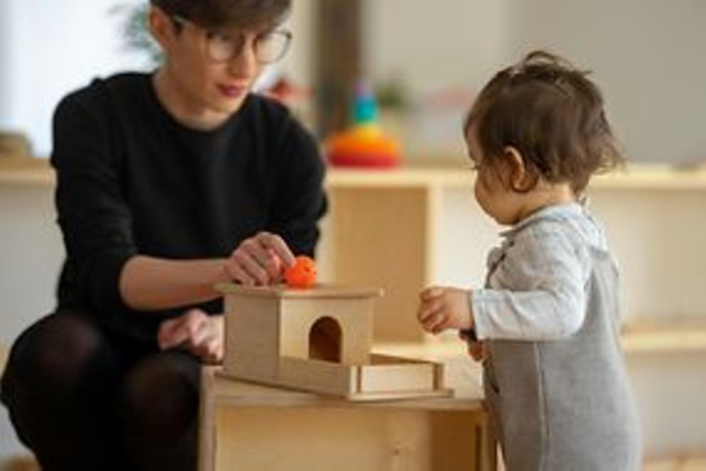 Sitzende Frau spielt mit Kleinkind und Holzspielzeug