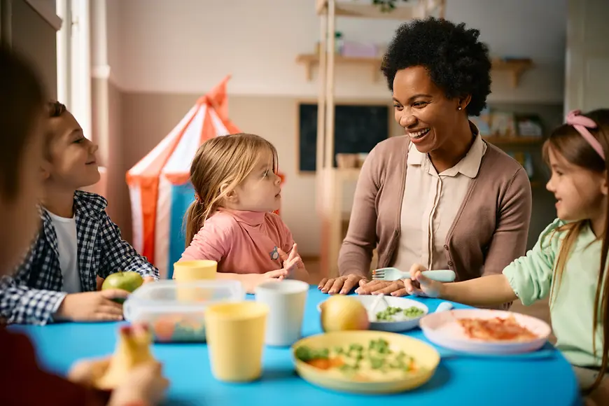 Frau sitzt mit Kindern am Mittagstisch und lacht.