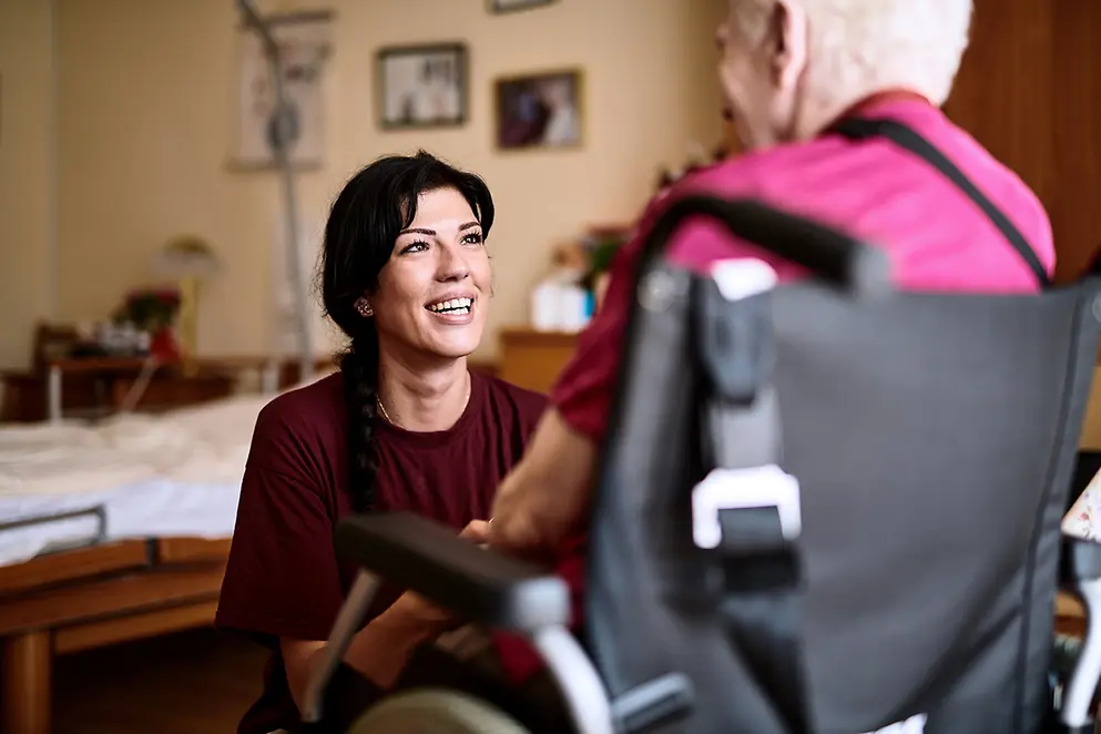 Eine junge Frau kniet vor einer älteren Frau im Rollstuhl